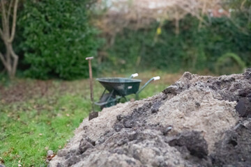 Construction work in the yard of a private home, a wheelbarrow a shovel and a pile of earth against the backdrop of a modern building 