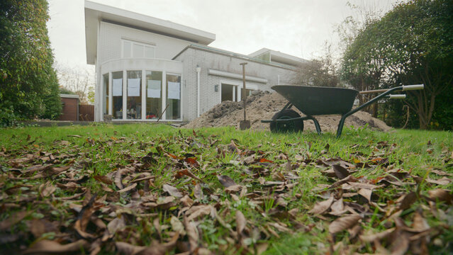 Construction work in the yard of a private home, a wheelbarrow a shovel and a pile of earth against the backdrop of a modern building 
