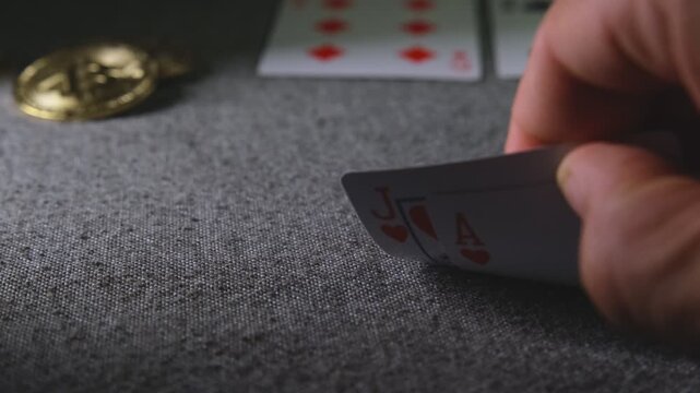 Hand checking ace and jack of hearts playing cards with bitcoin coins on a poker table