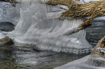 Icicles hang over a flowing river, capturing the contrast between the stillness of the ice and the movement of the water. The scene evokes a sense of tranquility and cold beauty.