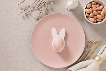 Elegant Easter table setting with pink plates, bunny shaped napkin ring and pastel egg. Modern spring holiday decor with soft light. Ccopy space.