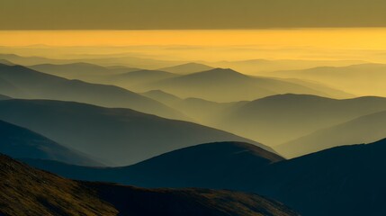 Fototapeta premium Sun-kissed mountain silhouettes layered against a golden hazy horizon at dawn or dusk