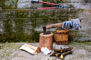 Firewood chopping setup outdoors with an axe stuck in a wooden stump, work gloves on the handle,...