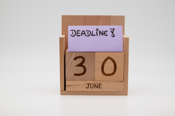 Wooden desk calendar showing 30th June with a handwritten deadline note on a paper card, symbolizing time pressure, planning, productivity, and end-of-month business tasks.