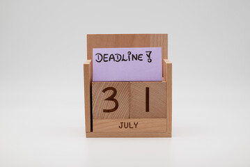 Wooden desk calendar showing 31st July with a handwritten deadline note on a paper card, symbolizing time pressure, planning, productivity, and end-of-month business tasks.
