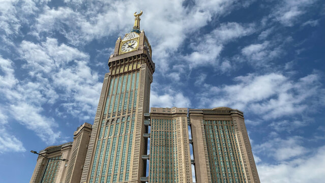Low-angle view of the Abraj Al Bait complex featuring the Makkah Clock Royal Tower, one of the world's tallest buildings, under a cloudy sky in Mecca, Saudi Arabia.