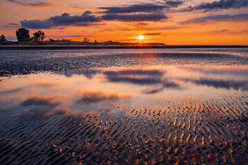 summer sunrise where the lagoon meets the sea with reflection of the clouds inside the puddles created by the tide, Bibione Pineda, Venice © fruttuoso