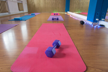 Unrolled pilates and yoga mat on wooden floor in fitness studio. Modern gym interior with equipment, daylight. Healthy lifestyle concept. Sports fitness equipment, women's, yoga blocks, dumbbells