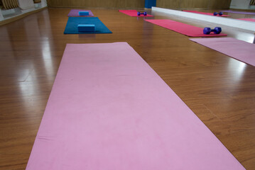Unrolled pilates and yoga mat on wooden floor in fitness studio. Modern gym interior with equipment, daylight. Healthy lifestyle concept. Sports fitness equipment, women's, yoga blocks, dumbbells