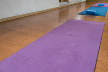 Unrolled pilates and yoga mat on wooden floor in fitness studio. Modern gym interior with equipment, daylight. Healthy lifestyle concept. Sports fitness equipment, women's, yoga blocks, dumbbells