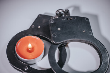 A burning orange tealight candle is placed in a black metal handcuff bracelet on a plain...