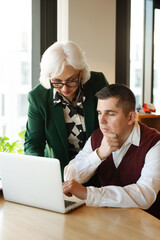Senior business mentor guiding colleague at laptop.