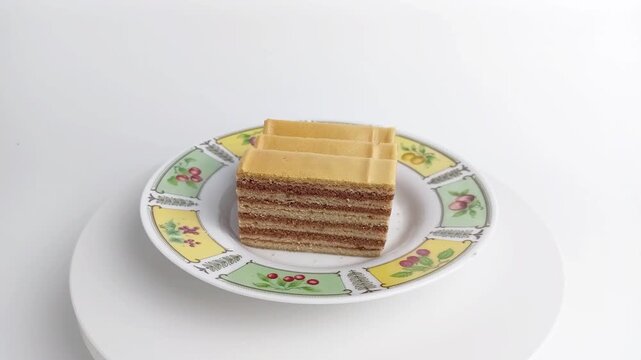Slices of lapis legit layer cake rotating on plate. Sweet traditional spekkoek or thousand layer cake. Indonesian dessert food concept.
