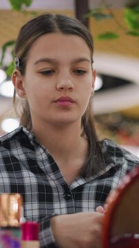 latina girl inspecting lipstick at counter, colorful bottle display and round mirror under bright retail lights, testing shade on hand and studying finish, boutique and mall backdrop, budding