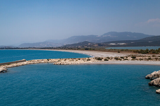 Sandy barrier island separates the sea from Beymelek Lagoon, with distant mountains and Demre city on green slopes. A calm, deserted coastal scene. Demre, Turkey, Mediterranean.

