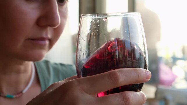 Closeup of a woman gently swirling a glass of red wine to release aroma before tasting. Focus on hand and glass with reflections, sommelier technique and elegant beverage lifestyle concept 