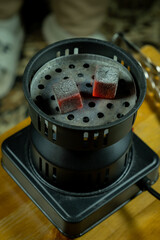 Hot coals placed in a hookah bowl on a wooden table during a social gathering in the evening