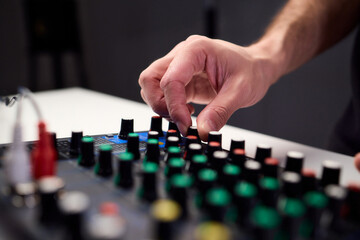 Naklejka premium Closeup of hands adjusting mixer with glowing LED indicators and cables, Detailed image of operator controlling mixer dials and monitoring sound through sensors and LEDs