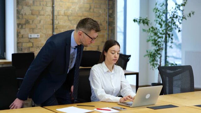 Woman sitting and working on computer in office, man colleague coming