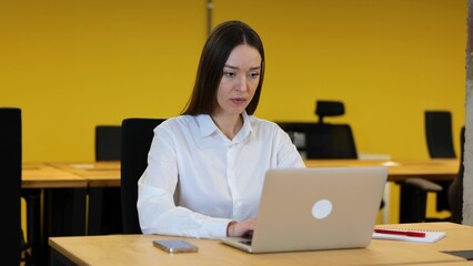 Caucasian woman in a white shirt and grey trousers is sitting on her working desktop in modern office. video