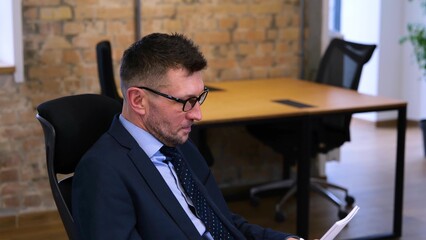 video. Caucasian middle age man s sitting on the table in front of computer and reading. Woman is...