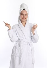 Beautiful woman with hair wrapped in towel holding jar of cream against white background