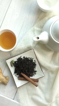 A finest quality tea served in a white porcelain cup placed along with teapot and Indian spices. A slow revolving shot from above angle. An Asian food photography.