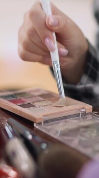 closeup brush dipping into palette, soft bristles lifting neutral shimmer from pans, manicured fingers guiding tool over compact, busy vanity foreground with brushes and case, studio camera setup,