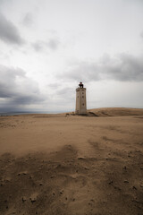 tall, weathered lighthouse, barren sand dunes, pale, overcast sky, minimalist, atmospheric coastal scene. olitude, timelessness, and navigation, travel, resilience, and remote landscapes., backlit