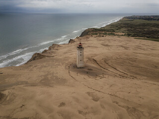 solitary lighthouse atop vast sand dunes, calm, expansive sea, dramatic, overcast skies. coastal landscape, isolation, resilience, and natural beauty, travel, navigation, moody seascapes.