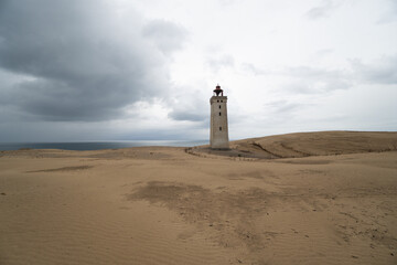 tall, weathered lighthouse, barren sand dunes, pale, overcast sky, minimalist, atmospheric coastal scene. olitude, timelessness, and navigation, travel, resilience, and remote landscapes., backlit