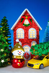 Fototapeta premium A snowman and a yellow car near a red Christmas house