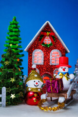 A snowman and a snowman on a sled with a gift near a red Christmas house