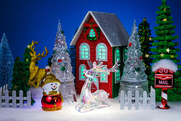 A snowman and a snowman on a white sled with a gift near a red Christmas house surrounded by a fence