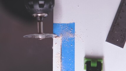 Close-up of a worker using a circular saw attachment on a drill to cut a white wooden board