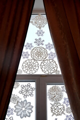 Decorative paper snowflakes hanging in a window, with sheer curtains framing the scene, creating a cozy winter atmosphere and showcasing intricate designs and patterns