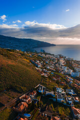 Aerial view of Funchal, Madeira, Portugal, terraced hillsides descend to the coastal city, a large vessel rests near the harbor, late afternoon light and clouds present. © Aerial Film Studio