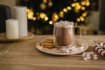 Holiday, Christmas background. A cup with hot chocolate and marshmallows on the table with Christmas tree on background