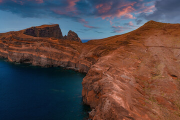 Aerial view of stratified volcanic cliffs at Ponta de Sao Lourenco, Madeira, warm side light reveals ridges and coves, deep blue Atlantic waters, jagged sea stacks nearby.