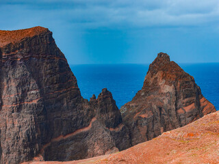 Dark lava cliffs with rusty bands rise above the Atlantic at Ponta de Sao Lourenco, Madeira. Daytime view from a high vantage point shows knife edged ridges and surf.