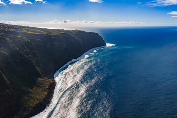 Aerial view of sea cliffs on Madeira north coast near Seixal and Sao Vicente, Portugal. Midday light, deep blue water, parallel swells strike dark basalt shore.