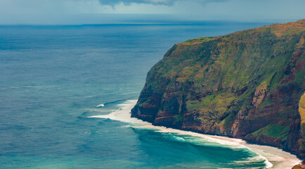 Towering green and rust cliffs drop to turquoise water in Madeira, Portugal, near Miradouro Farol da Ponta do Pargo, with white surf and soft diffused daylight.