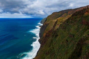 Layered volcanic cliffs meet the Atlantic on Madeira's northwest coast, white surf lines the rugged shore, soft daylight from a high vantage, cobalt waters extend.