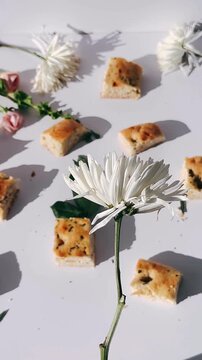 a white flower placed among small pieces of herb bread on a bright surface with natural shadows and soft organic details.