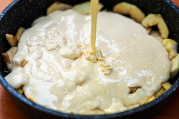 Thick light cream streaming into pan with sliced apples for making a pie