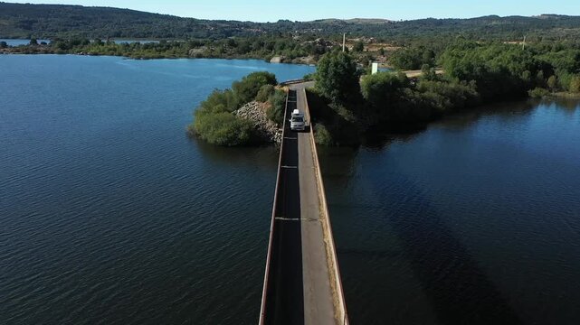 A camper minibus drives across a lake on a long, narrow bridge. Northern Portugal. 