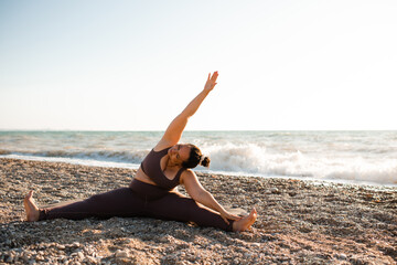 Woman 30-35 year old doing yoga stretching at beach over sea background outdoors. Healthy active lifestyle.