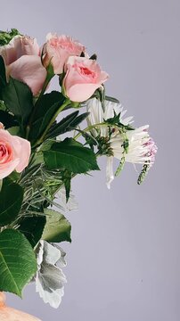 A gentle floral arrangement featuring blush pink roses, white chrysanthemum flowers, and textured green leaves against a light neutral background.