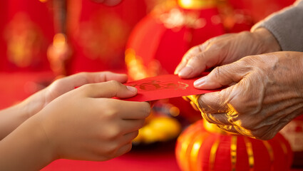 Close-up of elderly hands passing a red envelope to a child&rsquo;s hands during Chinese New Year celebration, symbolizing family tradition, blessings, prosperity and cultural heritage in warm festive light