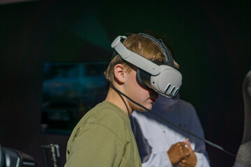 Child wearing VR headset focuses on immersive virtual reality experience, exploring modern gaming technology in dark indoor environment.